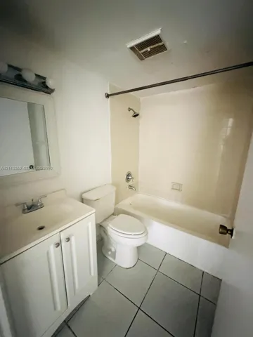 Bathroom featuring a white vanity cabinet, ceramic tile flooring, a tub and shower combination with tile surround, and a wall-mounted vanity mirror with integrated light fixture