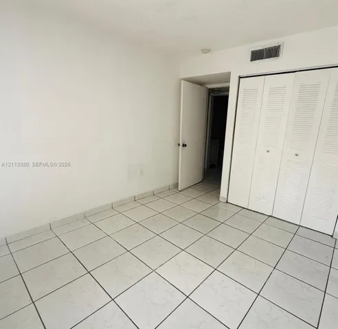 Neutral-toned ceramic floor tiling and full-height closet featuring white louvered bifold doors