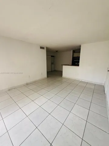 Open-concept interior featuring light-toned tile flooring and a kitchen breakfast bar with stone-surface countertop