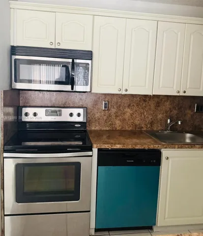 Kitchen featuring off-white raised-panel cabinetry, stone-finish countertops, stainless steel electric range, over-the-range microwave, and stainless steel undermount sink