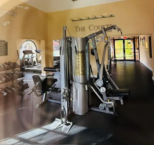Fitness center featuring rubber flooring, arched windows, and mounted lighting fixtures