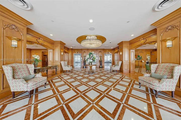 Grand lobby featuring intricate stone-inlay flooring, extensive wood-paneled walls, crystal tiered chandelier, recessed lighting, and arched openings