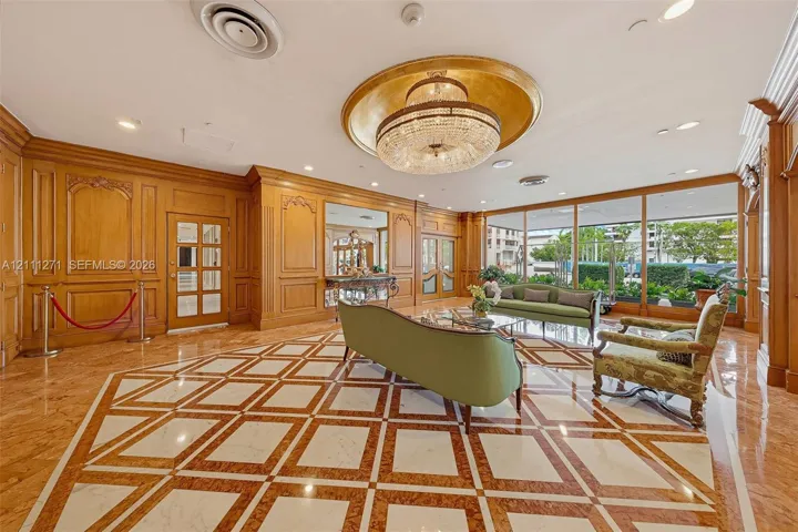 Grand lobby featuring wood-paneled walls, intricate geometric stone flooring, a large circular ceiling medallion, a tiered crystal chandelier, and floor-to-ceiling glass windows