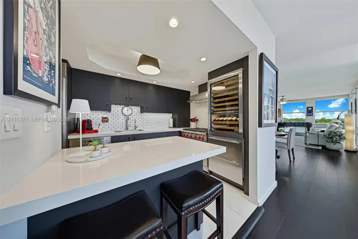 Kitchen featuring dark cabinetry, solid-surface breakfast bar, mosaic tile backsplash, stainless steel range, and built-in wine refrigeration