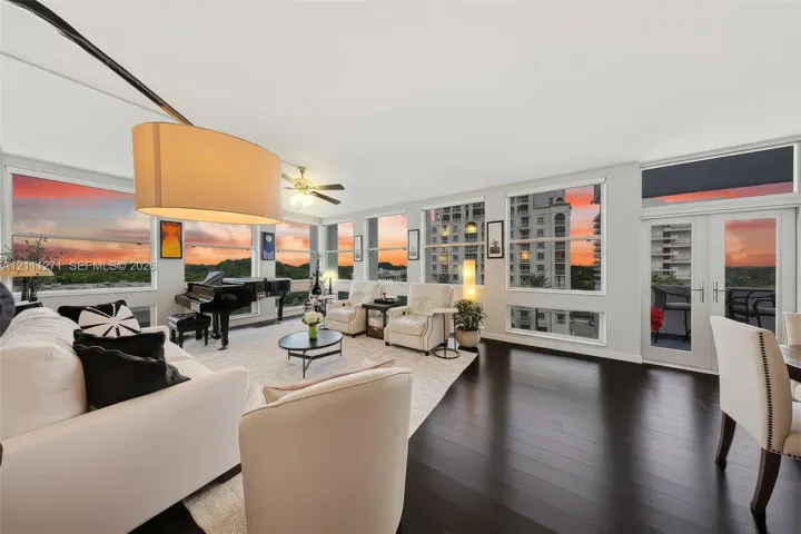 Living area featuring expansive window walls, dark wood-finish flooring, ceiling fan, and access to a private balcony