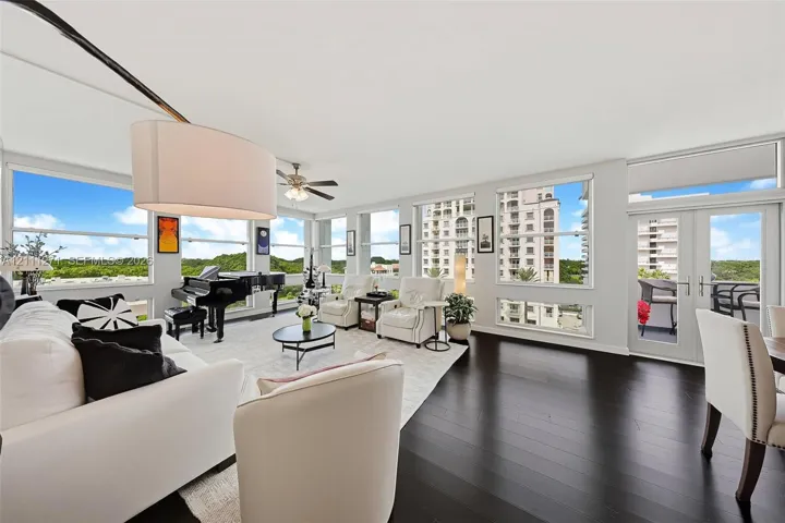Open-concept living area featuring dark wood-finish flooring, floor-to-ceiling windows, a ceiling fan, and double-glass doors leading to a balcony