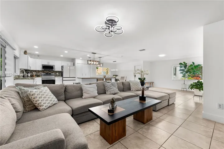 Open-concept living space featuring ceramic tile flooring, recessed lighting, modern geometric chandelier, and white cabinetry