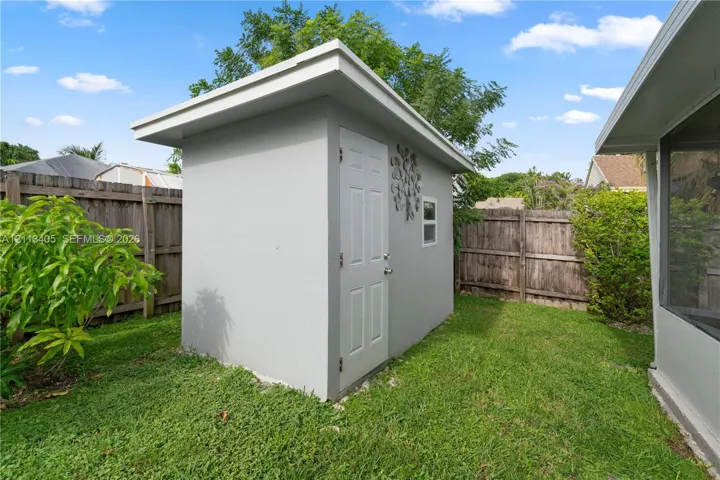 Detached exterior storage structure featuring a shed roof, light-colored smooth exterior finish, single-entry door, and window
