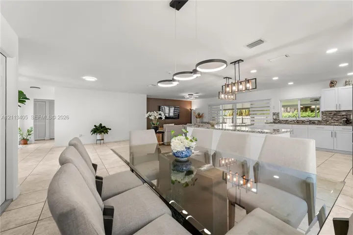Open-concept living space featuring ceramic tile flooring, recessed lighting, modern geometric pendant chandeliers, white shaker-style cabinetry, and a stone-tiled backsplash