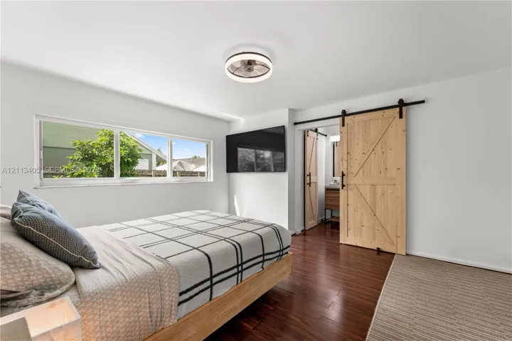 Wood-finish flooring, sliding wood barn door with matte black hardware, large picture window, and integrated circular ceiling fan with lighting