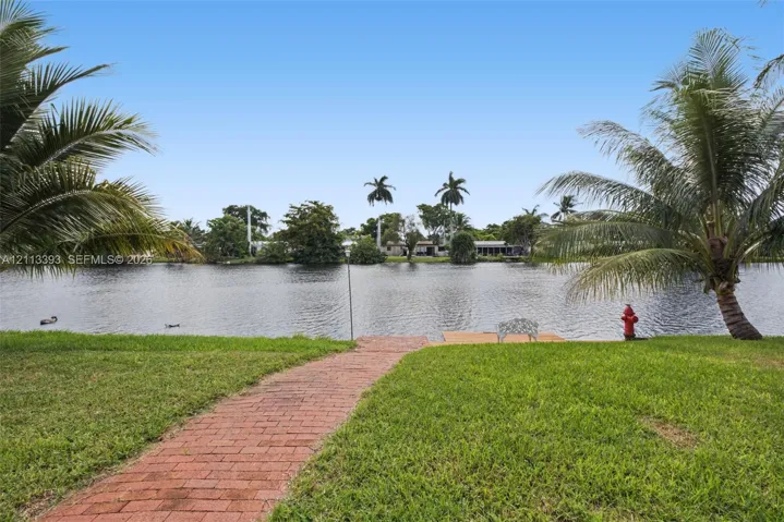 Waterfront parcel featuring a brick paver walkway, manicured lawn, and mature palm trees