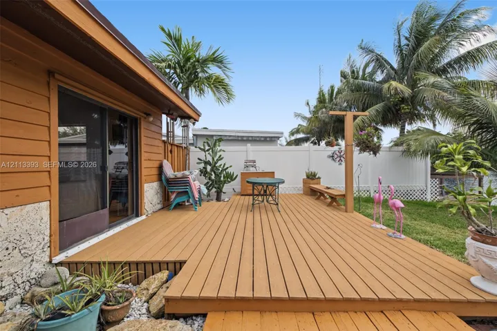 Raised wood-finish deck with sliding glass door access, stone veneer foundation, and white vinyl privacy fencing