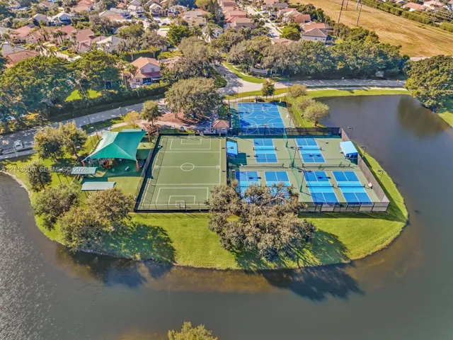 Recreational complex featuring multi-purpose sports courts, pickleball courts, a soccer field, and a shaded playground pavilion situated on a waterfront parcel