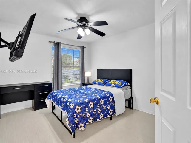 Room featuring wood-finish flooring, a matte black multi-blade ceiling fan with integrated lighting, a dual-pane window, and a multi-panel door with brass-finish hardware
