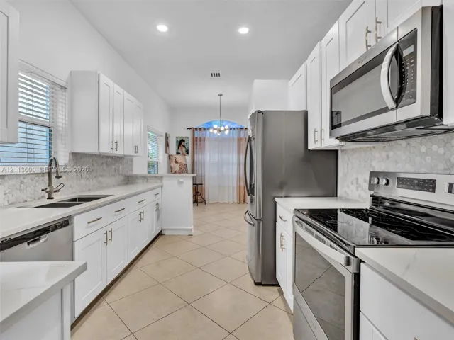 Kitchen featuring white shaker-style cabinetry, stainless steel appliances, quartz countertops, hexagonal mosaic tile backsplash, and tile flooring