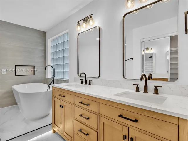 Double vanity featuring natural wood cabinetry, white stone-composite countertops, rectangular undermount sinks, and matte black fixtures