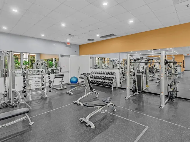 Fitness center featuring wall-to-wall mirrors, durable rubberized flooring, and recessed ceiling lighting
