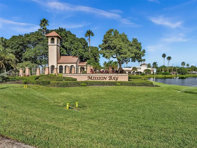 Stucco entry tower with tile roof, manicured landscaping, mature trees, and waterfront grounds