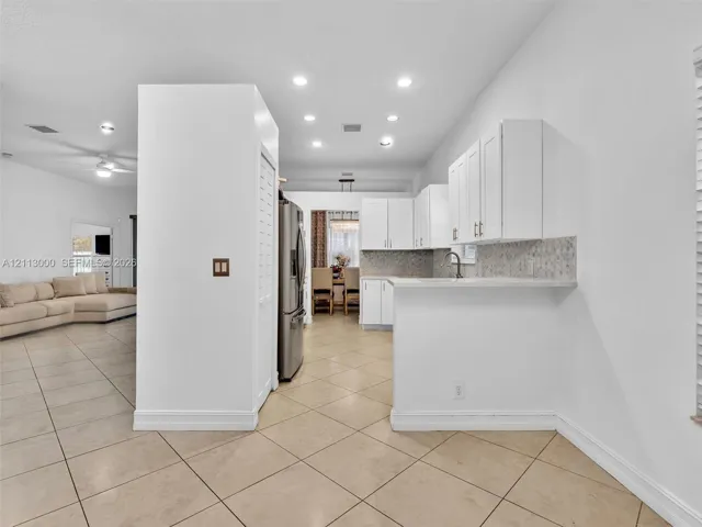 Kitchen featuring white cabinetry, solid-surface countertops, tile backsplash, stainless steel refrigerator, and recessed lighting