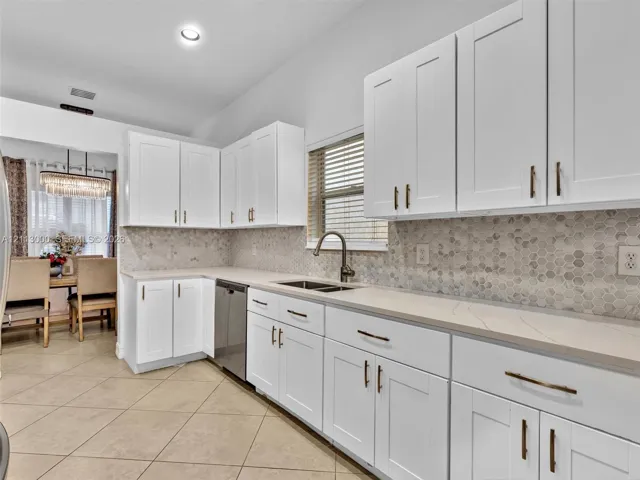 White shaker-style cabinetry with metallic pulls, stone-look countertops, hexagonal tile backsplash, stainless steel dishwasher, and a gooseneck kitchen faucet