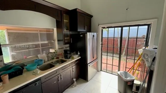 Kitchen featuring dark wood cabinetry, stainless steel appliances, solid surface countertops, a double-basin sink, and glass-paned sliding doors