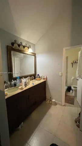 Dual-sink vanity with a stone countertop, stained wood cabinetry, a large framed mirror, and a multi-light fixture with glass shades