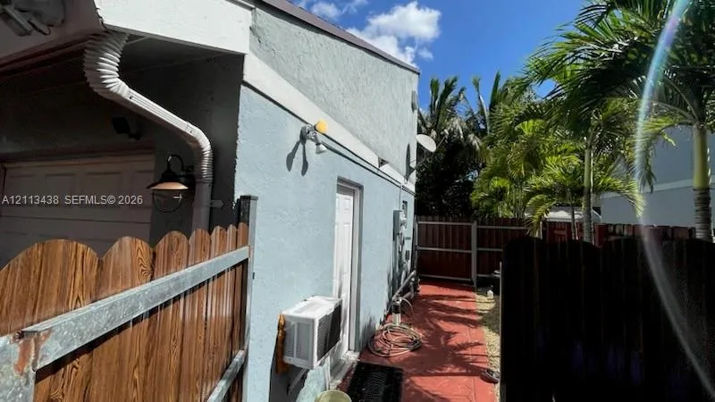Stucco exterior featuring an attached garage, a side entry door, exterior wall-mounted lighting, and a fenced side yard with paved walkway