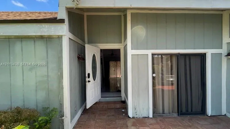 Exterior featuring board-and-batten siding, tile patio flooring, front door with oval glass insert, and sliding glass door with integrated screen