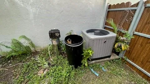 Exterior HVAC condenser unit mounted on a concrete pad, accompanied by a residential water treatment system and wood-finish privacy fencing