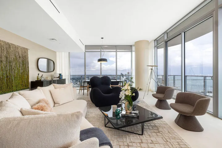 Floor-to-ceiling glass walls, sleek cylindrical architectural column, recessed linear lighting, polished neutral flooring, and integrated balcony access