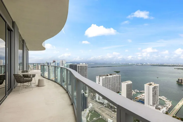 Curved balcony featuring a concrete floor, glass panel railing, and expansive water and skyline scenery