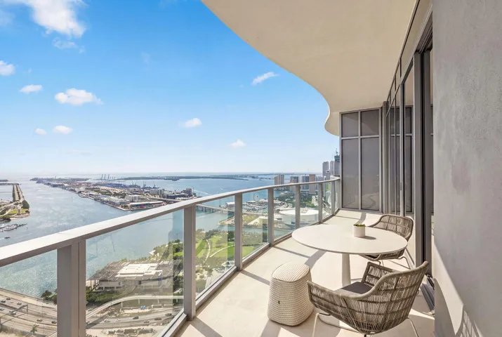 Covered balcony with a curved ceiling, glass panel railing, and expansive water and urban surroundings
