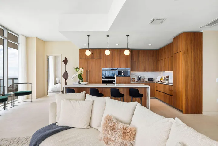 Modern kitchen featuring flat-panel wood cabinetry, a waterfall-edge kitchen island, stone backsplash, built-in wall oven, and three globe pendant lights
