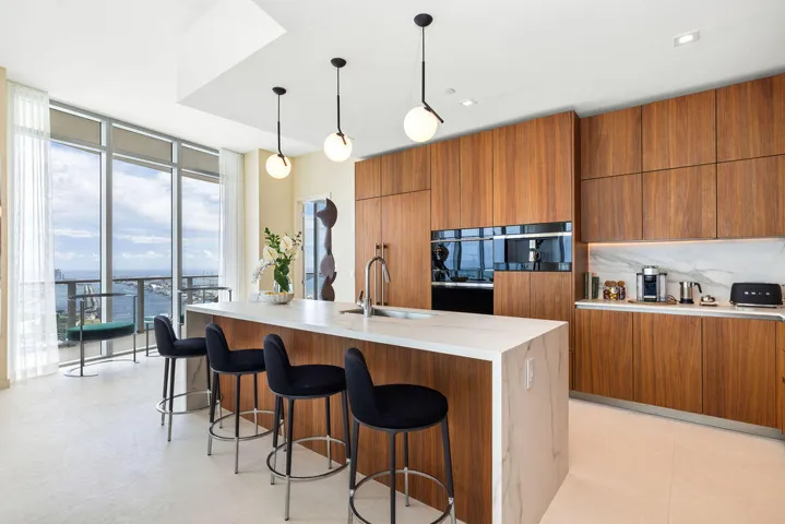 Kitchen featuring flat-panel wood cabinetry, stone-finish waterfall island with an undermount sink, built-in stainless steel appliances, and spherical pendant lighting