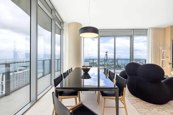 Floor-to-ceiling glass walls, wrap-around balcony with glass railing, cylindrical structural column, and modern pendant lighting