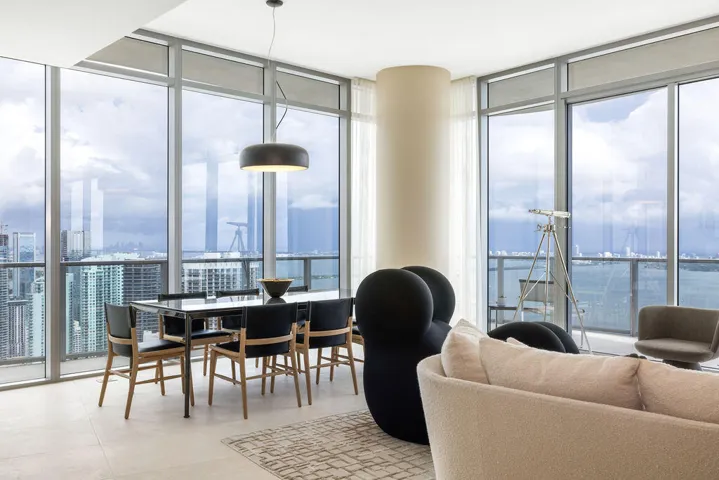 Floor-to-ceiling glass walls, wrap-around balcony with glass railing, large-format tile flooring, cylindrical structural column, and modern matte black pendant lighting