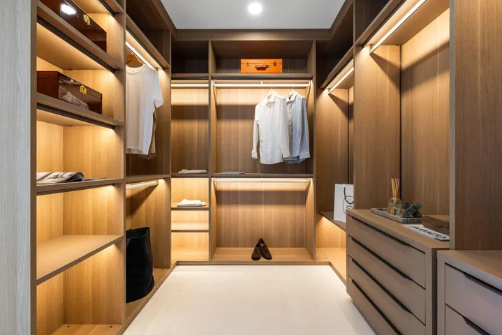 Custom closet featuring light wood-finish cabinetry, integrated LED shelf lighting, tiered hanging rods, and built-in dresser drawers with matte hardware