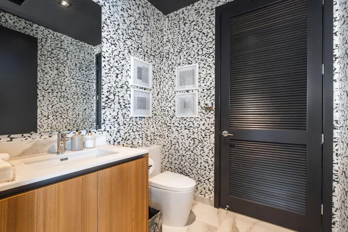 Floating wood-finish vanity with an integrated sink, large-scale wall mirror, patterned wall treatment, and black louvered door