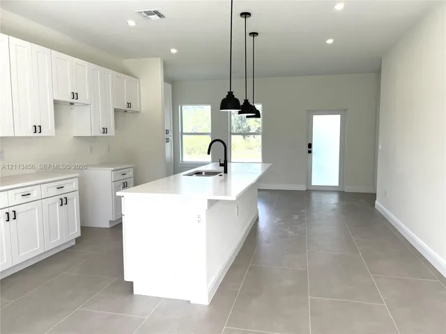 Kitchen featuring white cabinetry, an expansive center island with a stone-surface countertop, matte black faucet hardware, pendant lighting, and neutral-toned tile flooring