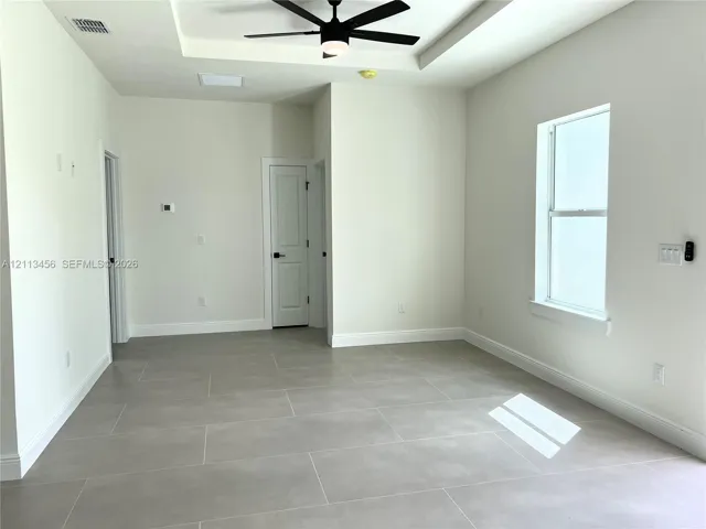 Tray ceiling featuring a central matte black ceiling fan, complemented by large-format neutral tile flooring and a vertical window