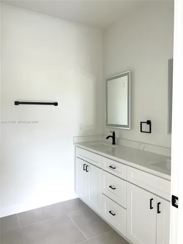Double-vanity cabinet with white shaker-style doors, stone-composite countertop, dual undermount sinks, matte black fixtures, and integrated mirror lighting