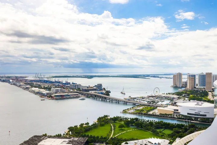 High-altitude perspective featuring expansive water frontage, bridge infrastructure, urban skyline, and a large manicured green space