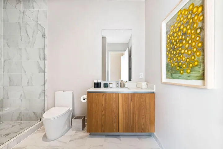Bathroom featuring a wood-finish vanity with a stone countertop, a glass-enclosed shower with large-format tile surround, a wall-mounted mirror, and tile flooring