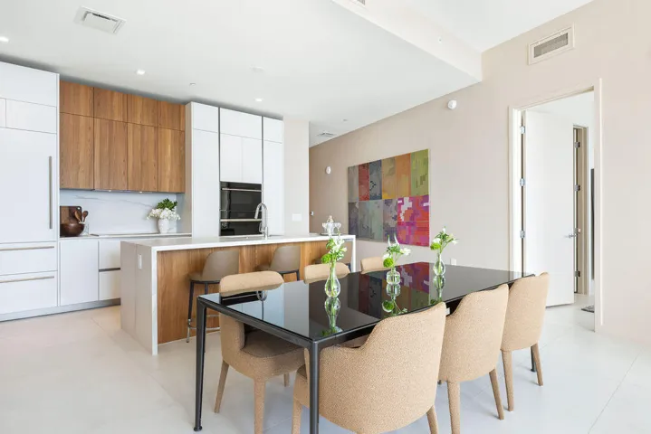 Modern kitchen featuring two-tone cabinetry with wood-finish uppers and white flat-panel base cabinets, central island with waterfall-edge countertop, integrated refrigerator, and built-in wall oven