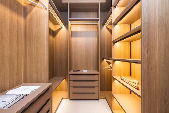 Custom walk-in closet featuring floor-to-ceiling wood-finish cabinetry, integrated linear task lighting, built-in drawer units, and open shelving