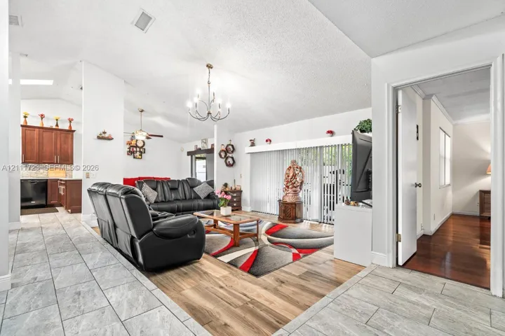 Open-concept living space featuring vaulted ceilings, wood-finish flooring, ceramic tile flooring, a multi-arm chandelier, and sliding glass doors