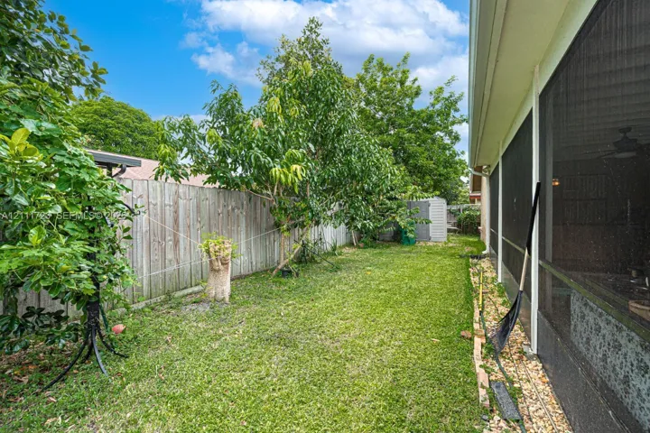 Rear yard featuring a grass lawn, mature trees, wood privacy fencing, and a screened enclosure