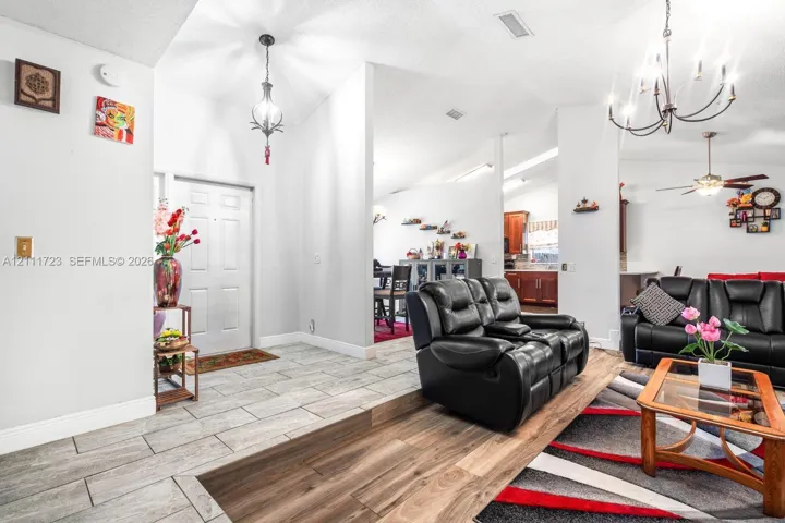 Open interior featuring vaulted ceilings, light-tone ceramic tile flooring, wood-finish flooring, and multi-arm chandelier lighting