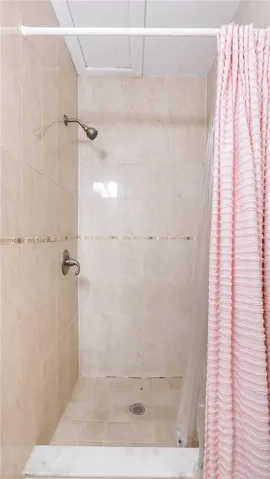 Walk-in shower featuring beige wall and floor tile, a decorative mosaic tile accent border, and a metallic shower fixture