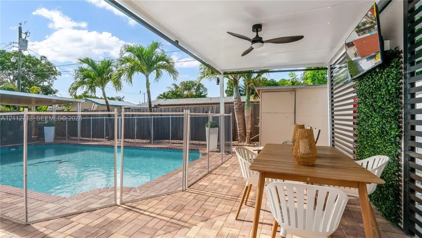 Covered patio featuring a ceiling fan, paver flooring, horizontal slat wall, and attached vertical garden wall, leading to a swimming pool with a safety enclosure